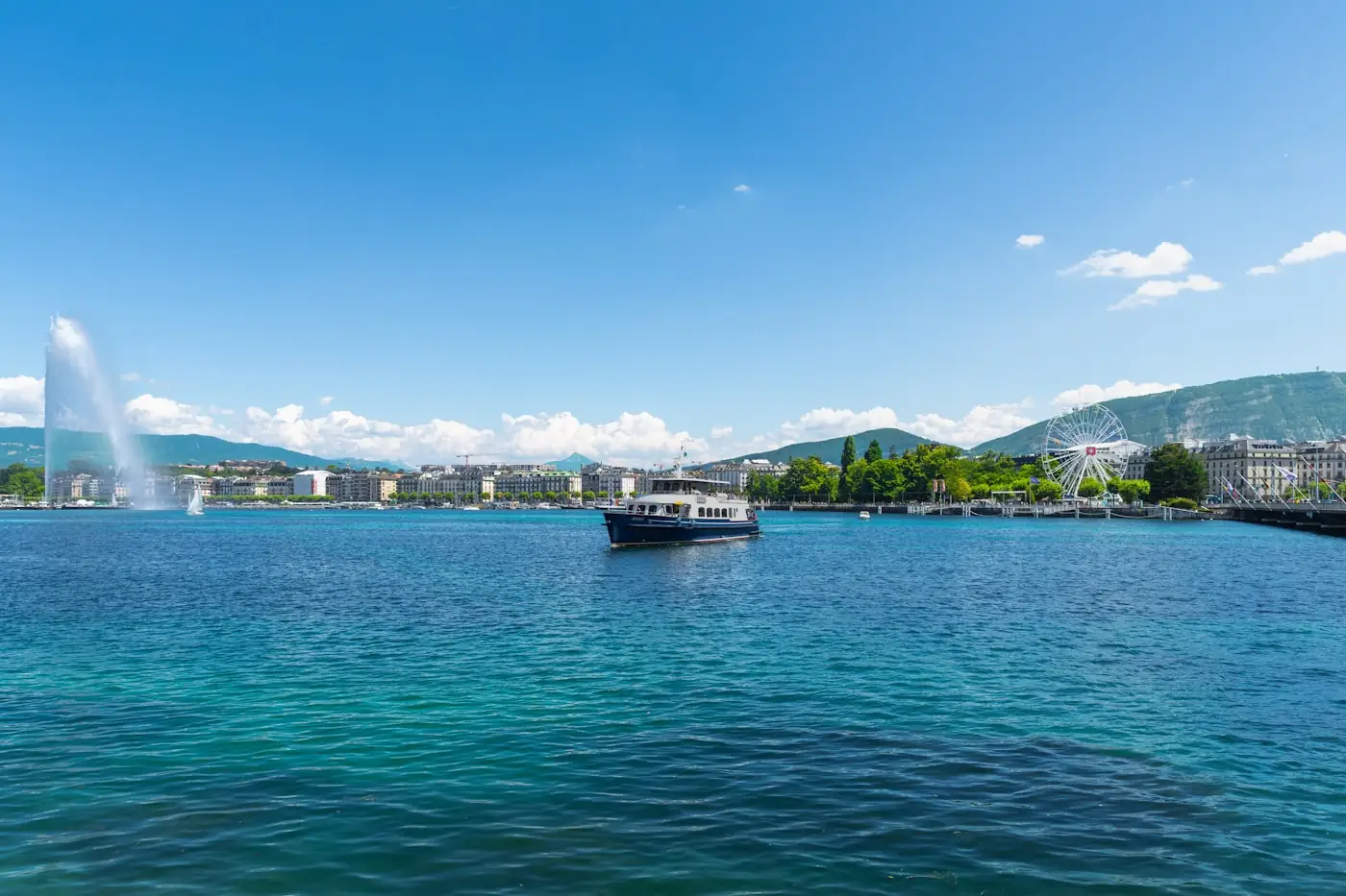 A boat crossing Lake Geneva with the Jet d'Eau and mountains behind